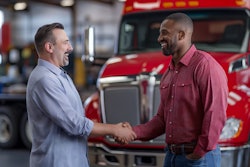 Two professionals shaking hands near a red commercial truck in a workshop