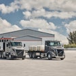 Two Volvo semi-trucks parked in front of a gray industrial warehouse