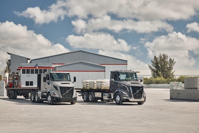 Two Volvo semi-trucks parked in front of a gray industrial warehouse