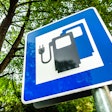 Blue road sign showing electric vehicle charging station symbol near trees