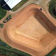 Aerial view of large earthen mound at industrial site with surrounding green landscape