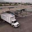 White Velocity delivery truck at logistics facility with concrete barriers and mountains in background