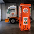 Orange electric truck parked next to bright orange EV charging station in industrial garage
