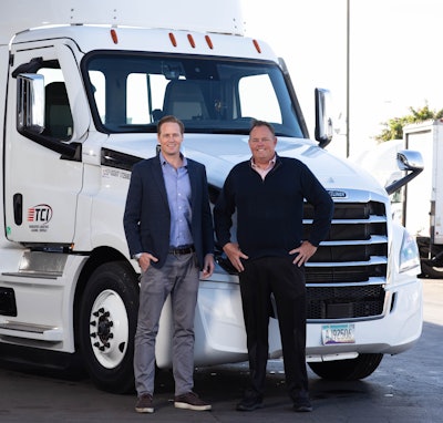 Two businessmen standing beside a white Freightliner semi-truck with TCI logo