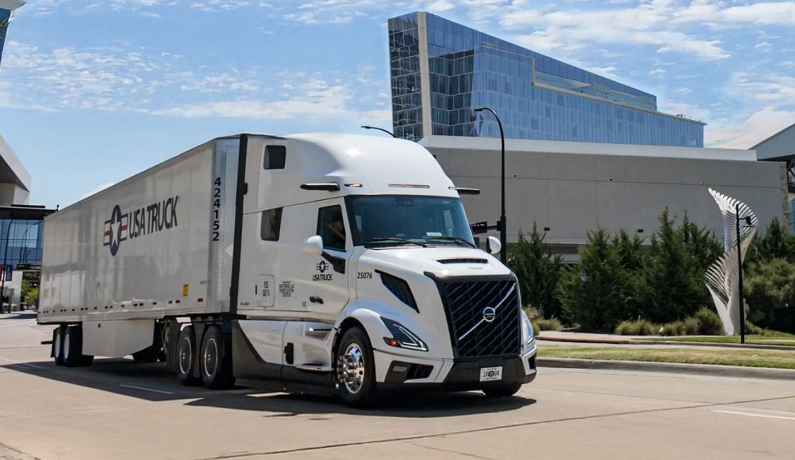 White Volvo semi-truck with trailer parked on urban street near modern glass building