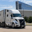 White Volvo semi-truck with trailer parked on urban street near modern glass building