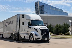 White Volvo semi-truck with trailer parked on urban street near modern glass building