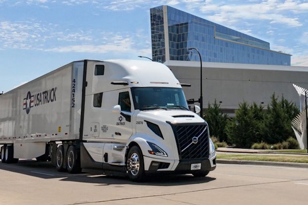 White Volvo semi-truck with trailer parked on urban street near modern glass building