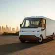 White electric delivery van parked with Los Angeles skyline at sunrise