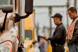 Transportation worker in safety vest checking truck documentation at vehicle inspection point