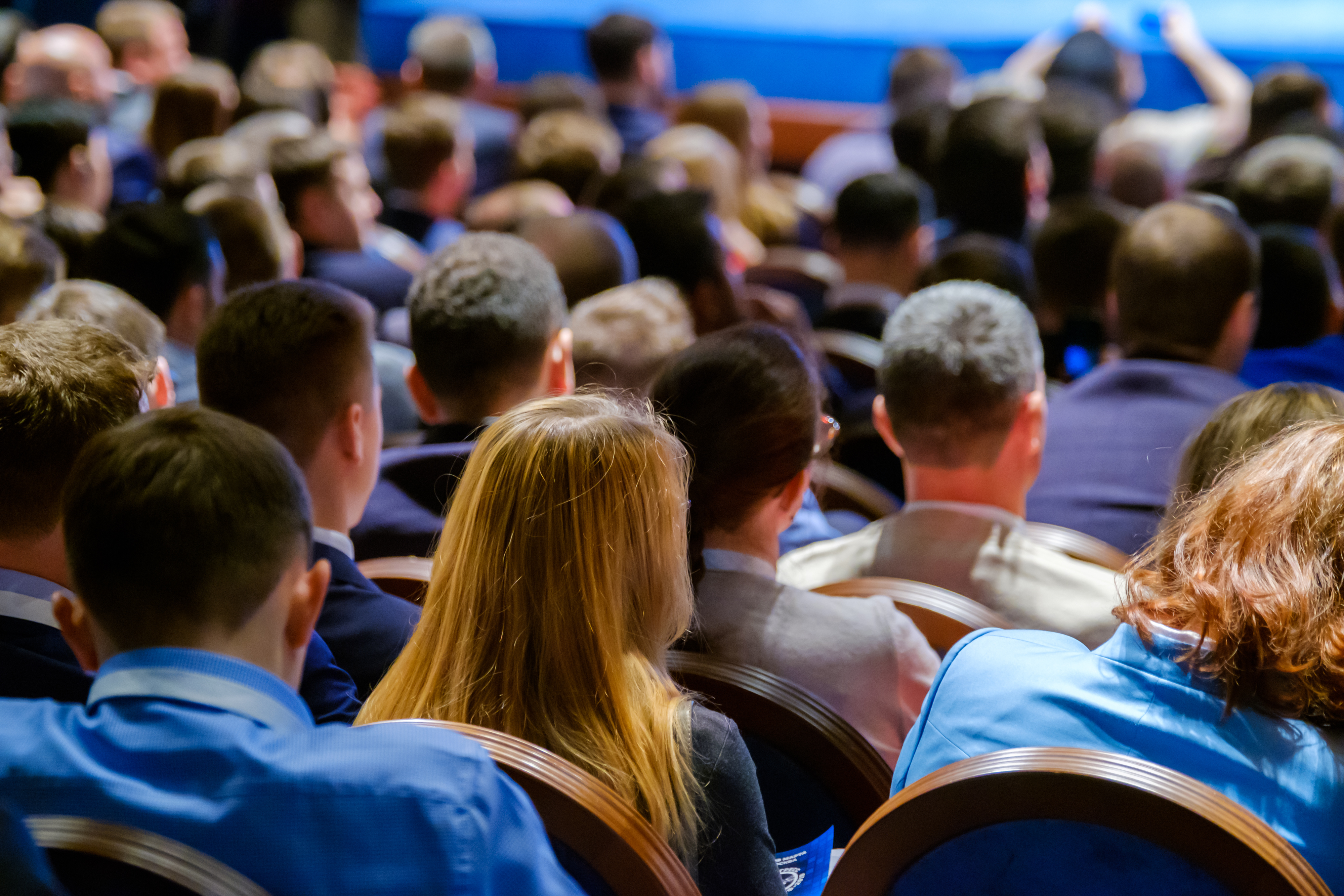 Crowd of professionals seated at conference, viewed from behind