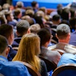 Crowd of professionals seated at conference, viewed from behind