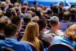 Crowd of professionals seated at conference, viewed from behind