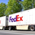 FedEx freight semi-trucks driving on a tree-lined highway