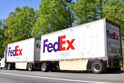 FedEx freight semi-trucks driving on a tree-lined highway