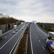 Multi-lane highway with trucks and cars under cloudy sky, noise barrier on left side