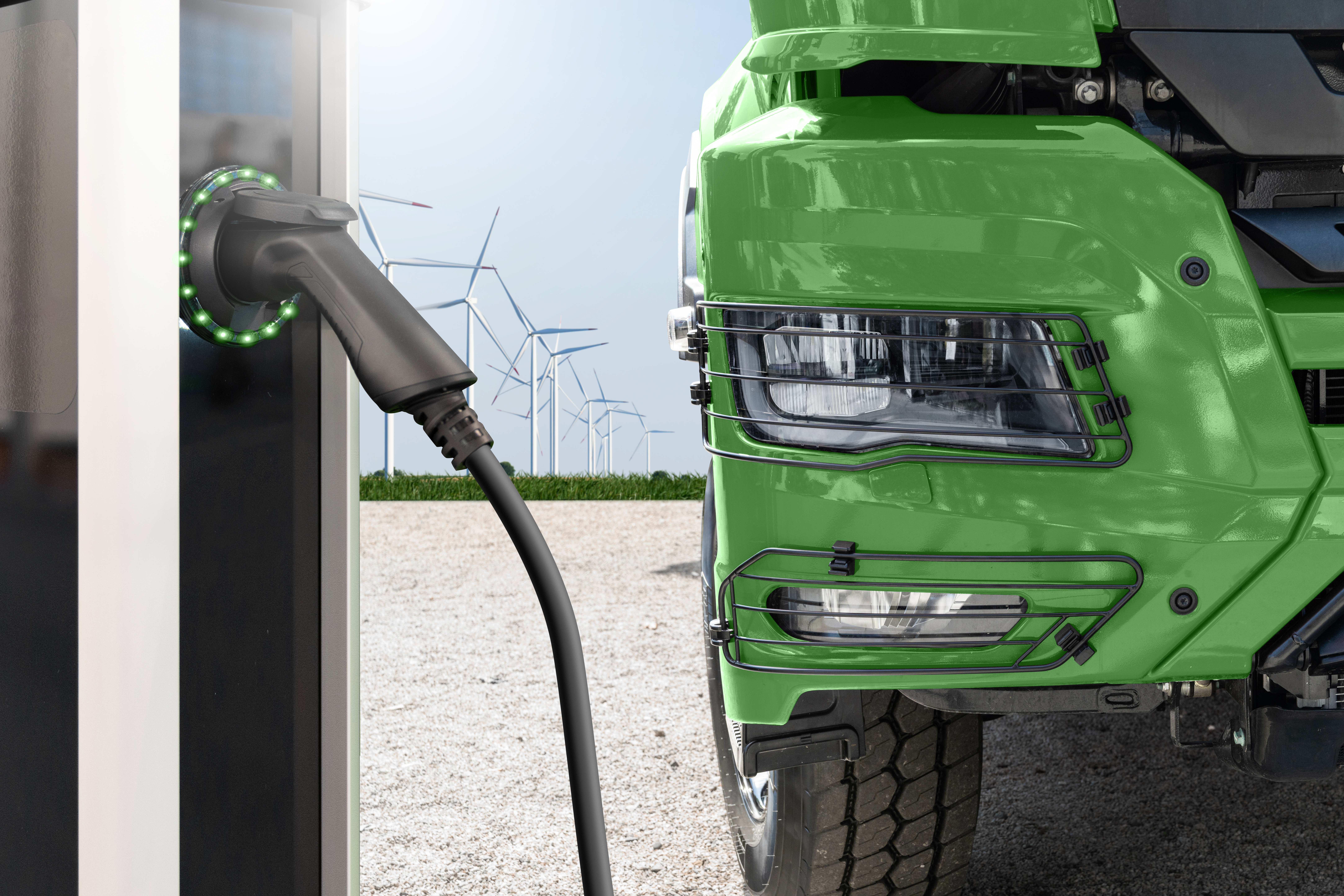 Green electric truck charging at station with wind turbines in background