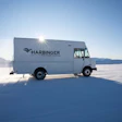 White Harbinger delivery truck parked on snow-covered ground with sunburst