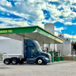 Blue semi-truck refueling at green hydrogen fuel station under cloudy blue sky