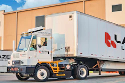 An Orange EV yard tractor hauling a Lazer Logistics trailer at a loading dock.
