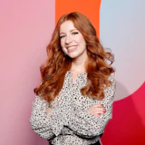 Smiling woman with wavy auburn hair in spotted blouse against colorful background