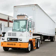 White and orange electric truck with trailer in industrial parking lot
