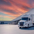 White semi-truck parked at loading dock during dramatic sunset with orange and blue sky