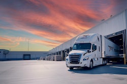 White semi-truck parked at loading dock during dramatic sunset with orange and blue sky
