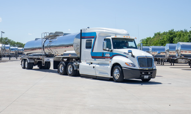 White and blue tanker truck with silver trailer parked on concrete lot
