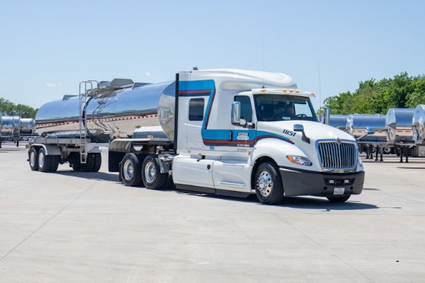White and blue tanker truck with silver trailer parked on concrete lot