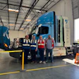 Four workers standing near a blue Symbio hydrogen truck in an industrial warehouse