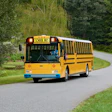 Yellow school bus driving on a curved road through a green forest landscape