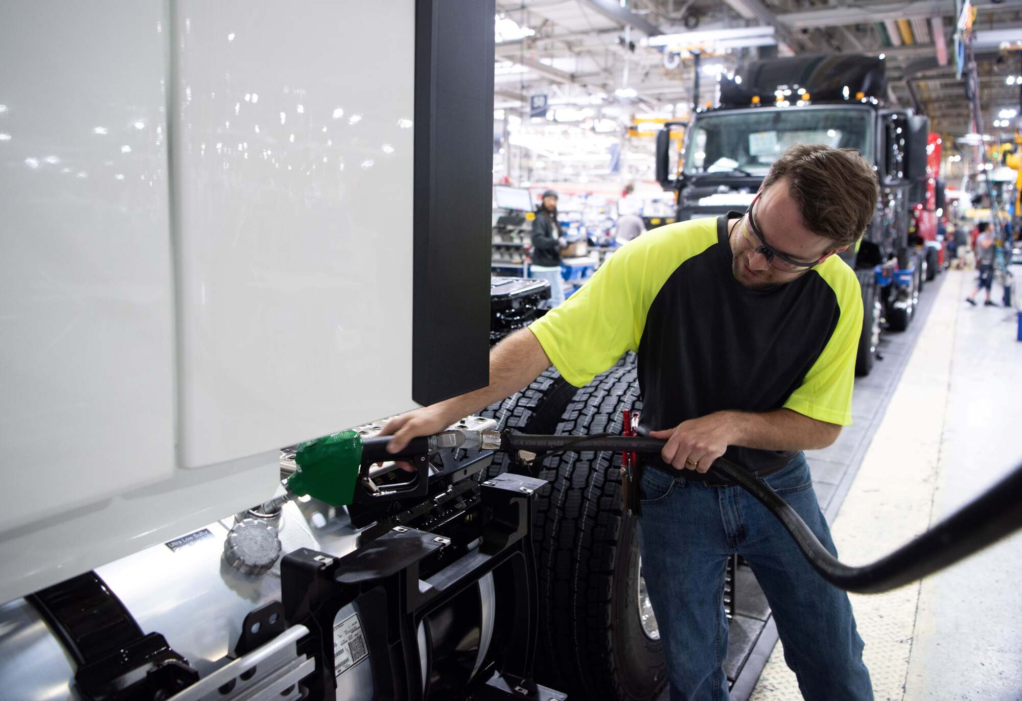 Worker in safety vest checking truck tire in industrial manufacturing facility