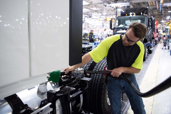 Worker in safety vest checking truck tire in industrial manufacturing facility