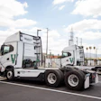 White electric semi-trucks with green WattEV branding charging at a commercial charging station