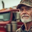 Weathered truck driver in camouflage cap with red truck in background