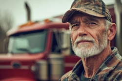 Weathered truck driver in camouflage cap with red truck in background
