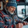 Truck driver in blue knit hat writing in notebook while seated in vehicle cab