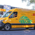Yellow DHL delivery van parked on street with trees and building in background