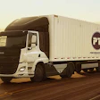 White semi-truck with Performance Team trailer driving on desert highway at sunset