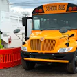 Yellow school bus parked next to green electric charging station with red safety barrier