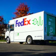 White Harbinger electric delivery truck with FedEX livery parked on street with autumn trees
