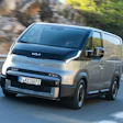 Silver Kia electric van driving on mountain road with rocky background