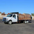 White commercial flatbed truck parked in an empty parking lot with suburban houses in background