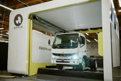 A Mitsubishi Fuso battery-electric truck is shown having its depleted battery replaced with a fully charged one at an Ample battery swapping station, a process which takes about five minutes.