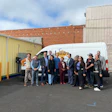 Group of professionals posing beside a white laundry service van in parking lot