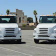 Two white commercial trucks parked side by side in an empty parking lot