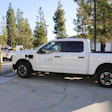 White electric pickup truck charging at an EV station with pine trees in background