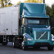 Teal Volvo semi-truck with white trailer parked on street near trees