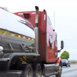 Red semi-truck with tanker trailer driving on highway with other vehicles